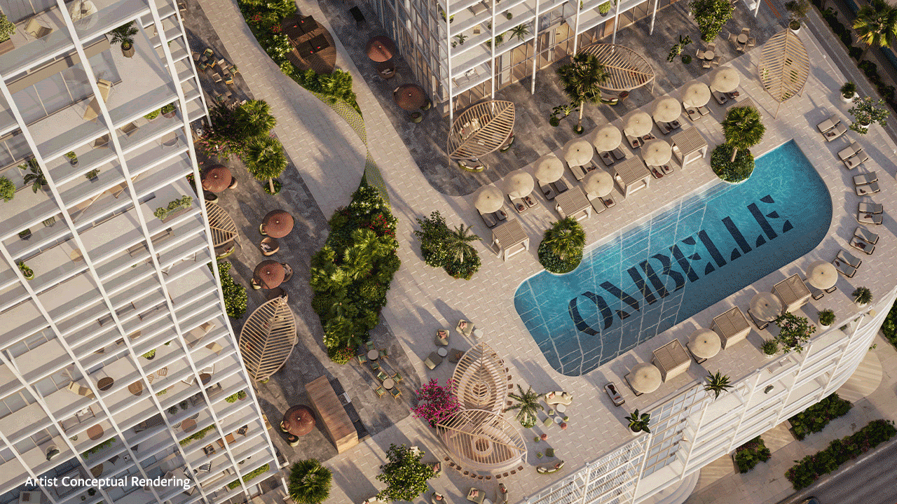 Aerial view of a modern outdoor pool area at Ombelle in Flagler Village, surrounded by lounge chairs, cabanas, palm trees, greenery, and curved walkways between tall white buildings. People are relaxing throughout the space, truly living well. Lifestyle