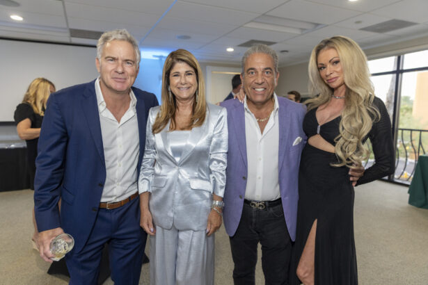 Four adults pose together at an indoor event. The two Men of Influence wear suits; one woman wears a shiny silver outfit, and the other wears a glamorous black dress with a high slit. All are smiling at the camera, celebrating Women of Influence 2025. Lifestyle