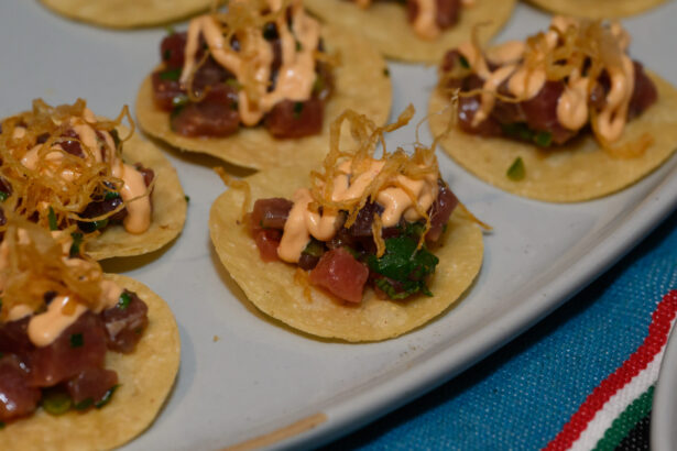 Small round tortilla chips topped with diced tuna, chopped herbs, creamy orange sauce, and crispy fried onions—an After Hours snack done right, arranged beautifully on a light-colored plate. Lifestyle