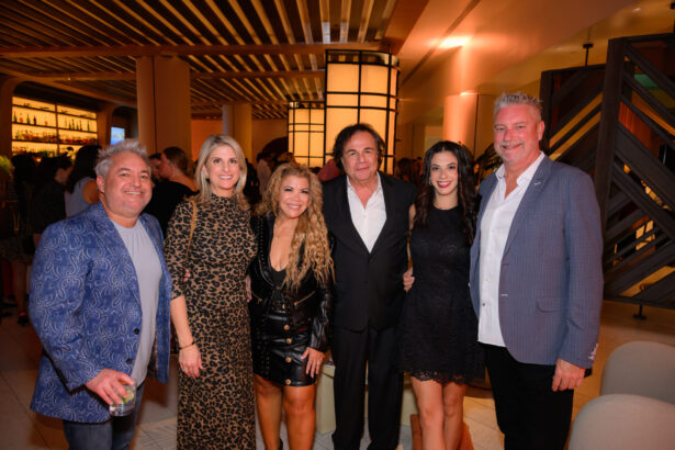 Six adults stand together, smiling for a group photo at an after hours event. They are dressed in semi-formal to formal attire, with warm lighting and a stylish, modern interior in the background—celebration done right. Lifestyle