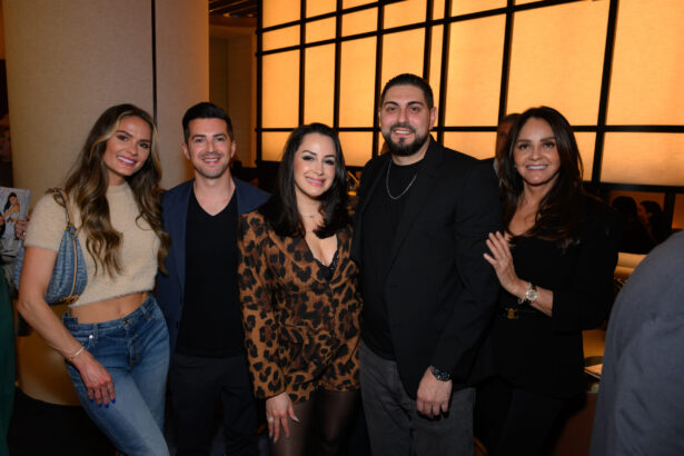 Five people pose together indoors, smiling at the camera during an After Hours event. The group includes three women and two men in stylish, semi-formal attire, standing before a softly backlit wall. Lifestyle