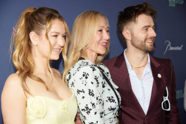 Three smiling people stand side by side at an event. The woman on the left wears a light yellow dress, the woman in the center wears a floral dress, and the man on the right paces himself confidently in a maroon suit with a white shirt. Lifestyle