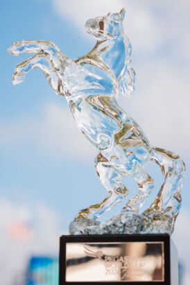 A crystal trophy shaped like a rearing Pegasus stands on a base inscribed with "Pegasus World Cup 2024," set against a soft, cloudy sky—capturing the pace and elegance of a new decade in racing. Lifestyle