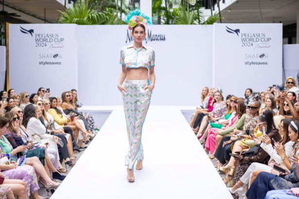 A model walks down a runway wearing a colorful crop top and matching pants, with a large floral headpiece—capturing the latest fashion trends. The audience sits on both sides of the white runway at the Pegasus World Cup 2024 fashion event. Lifestyle