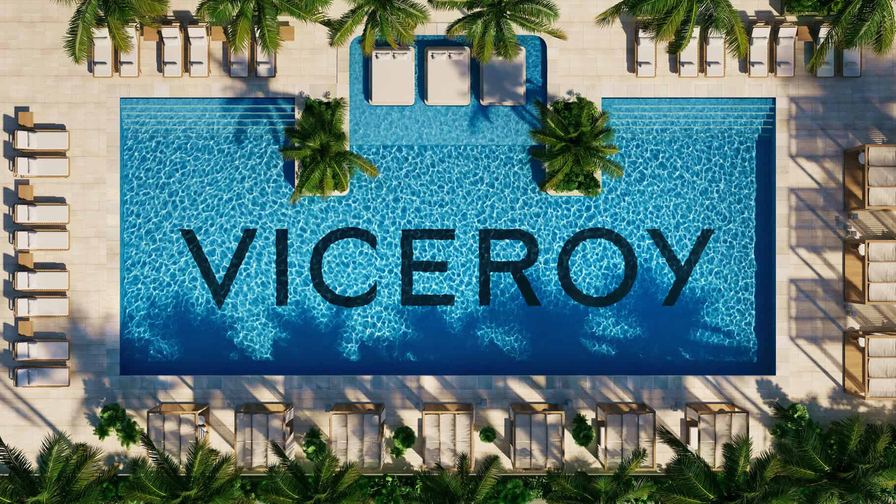 Aerial view of a rectangular swimming pool with "VICEROY" on its floor, surrounded by lounge chairs, umbrellas, and palm trees. Two poolside beds and small palm islands float in the water, creating a tranquil oasis like a river of relaxation—perfect for enjoying Pineapple Jam. Lifestyle