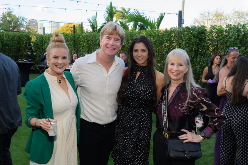 Four people pose together outdoors at the Palm Garden Event House’s March Event, smiling at the camera in semi-formal attire. Other guests mingle under string lights and lush greenery, capturing the lively Cover Party atmosphere. Lifestyle