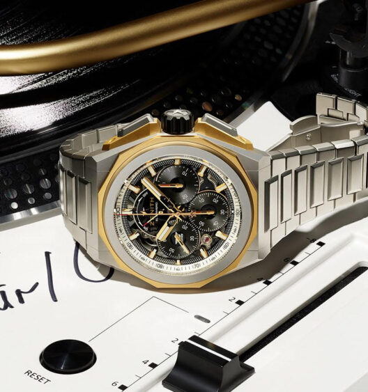 A luxury wristwatch with a metallic band and gold accents rests on a vinyl record player, its intricate black and gold skeleton dial echoing wrist frequency amidst music-related details. Lifestyle