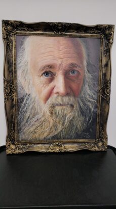 A realistic painting titled "Flesh and Canvas" depicts an elderly man with a long white beard and blue eyes, elegantly set in an ornate, antique-style gold frame against a plain background. Lifestyle