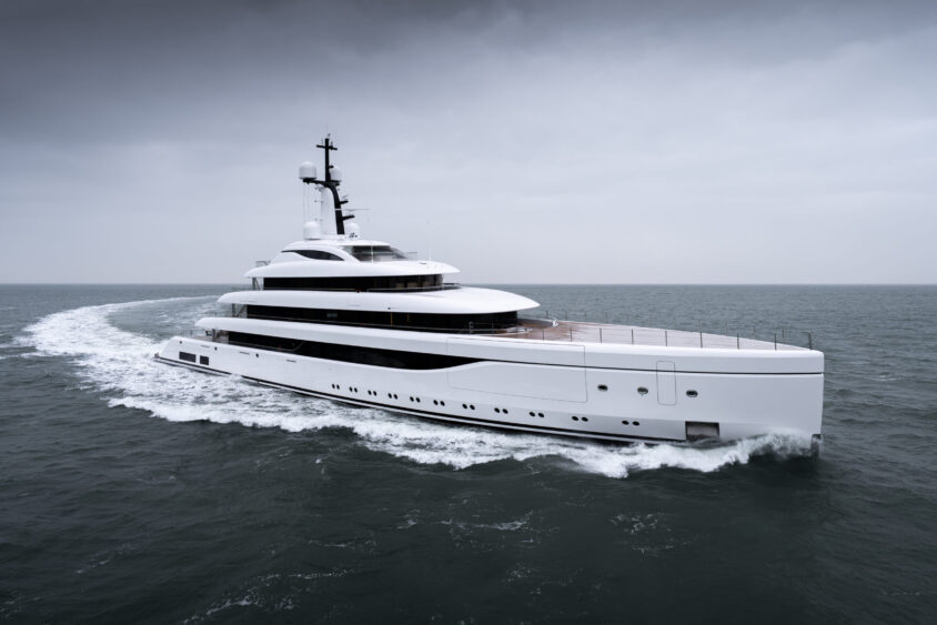 A large, modern white yacht cruises through calm, open water on a cloudy day, leaving a curved wake behind it—a fitting scene as the Century Marks vessel glides beneath an overcast sky across the expansive sea. Lifestyle