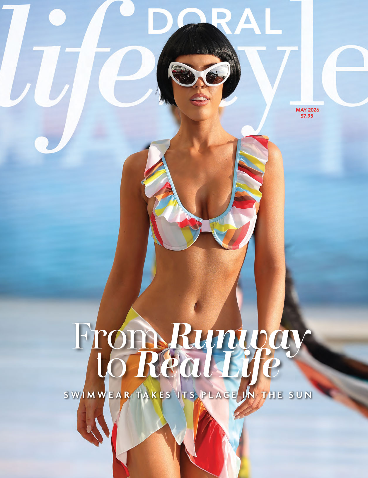 A model in a colorful ruffled bikini and white sunglasses walks the runway on the May 2026 cover of Doral Lifestyle magazine, with the headline "From Runway to Real Life: Swimwear Takes Its Place in the Sun. Lifestyle