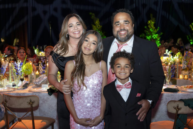 A smiling family of four poses together at a formal event, dressed elegantly in suits and dresses, embodying the spirit of Golden Angels amid decorated tables and guests in the background. Lifestyle