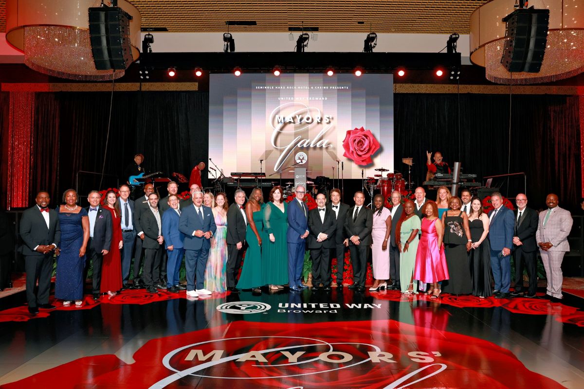 A large group of people in formal attire pose together on stage in front of a "Mayor's Gala" sign with a red rose design; the floor features the event’s logo and “United Way Broward,” highlighting their commitment to community impact. Lifestyle