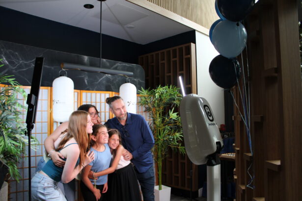 Five people smile and pose together for a photo in front of a photo booth at Ukiah Celebrates First Anniversary, standing in a well-lit indoor space decorated with plants, balloons, and lantern-style lights. Lifestyle