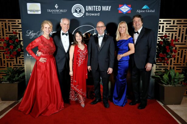 Six adults dressed formally stand together on a red carpet at the Mayors' Gala in front of a backdrop with logos, including United Way Broward, celebrating housing initiatives. Three women wear long gowns and three men wear black tuxedos, all smiling toward the camera. Lifestyle