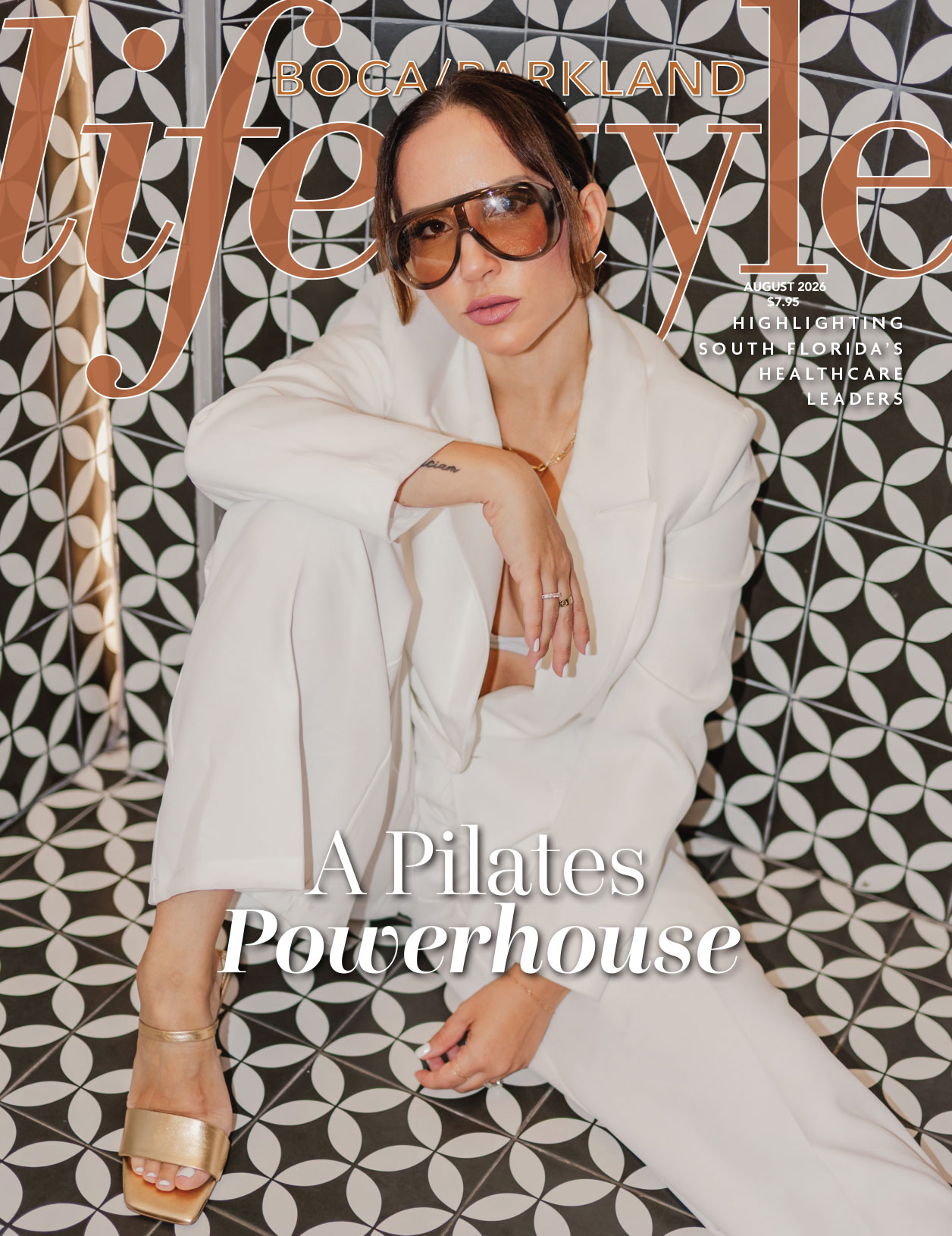 A woman in a white suit and sunglasses sits on patterned floor tiles, posing confidently for the cover of "Boca/Parkland Lifestyle" magazine, with the headline "A Pilates Powerhouse." Her poised demeanor perfectly embodies the vibrant Boca lifestyle. Lifestyle