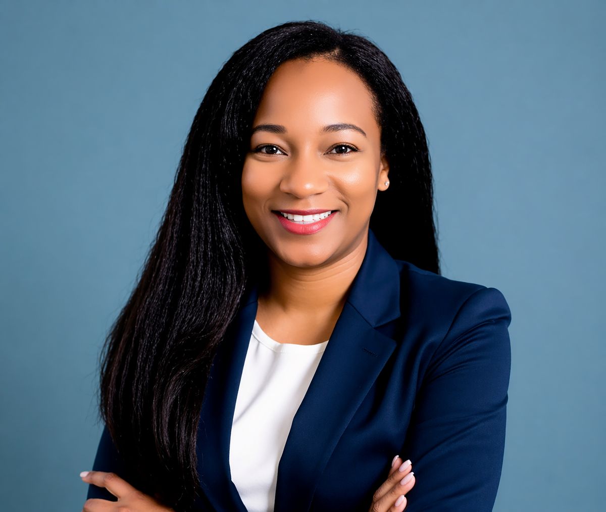 Shea S. Spencer, Chief Executive Officer of 211 Broward, stands confidently with arms crossed, her long, straight black hair cascading over a navy blazer and white top as she smiles in front of a plain blue background. Lifestyle
