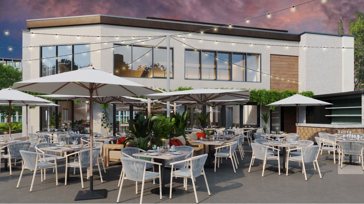 Outdoor restaurant patio with white umbrellas, string lights overhead, modern white chairs, and tables set for dining. A contemporary building with large windows serves as the backdrop, while lush plants decorate the seating area—creating an inviting atmosphere reminiscent of a Sunday in the Park at Sweetwaters. Lifestyle