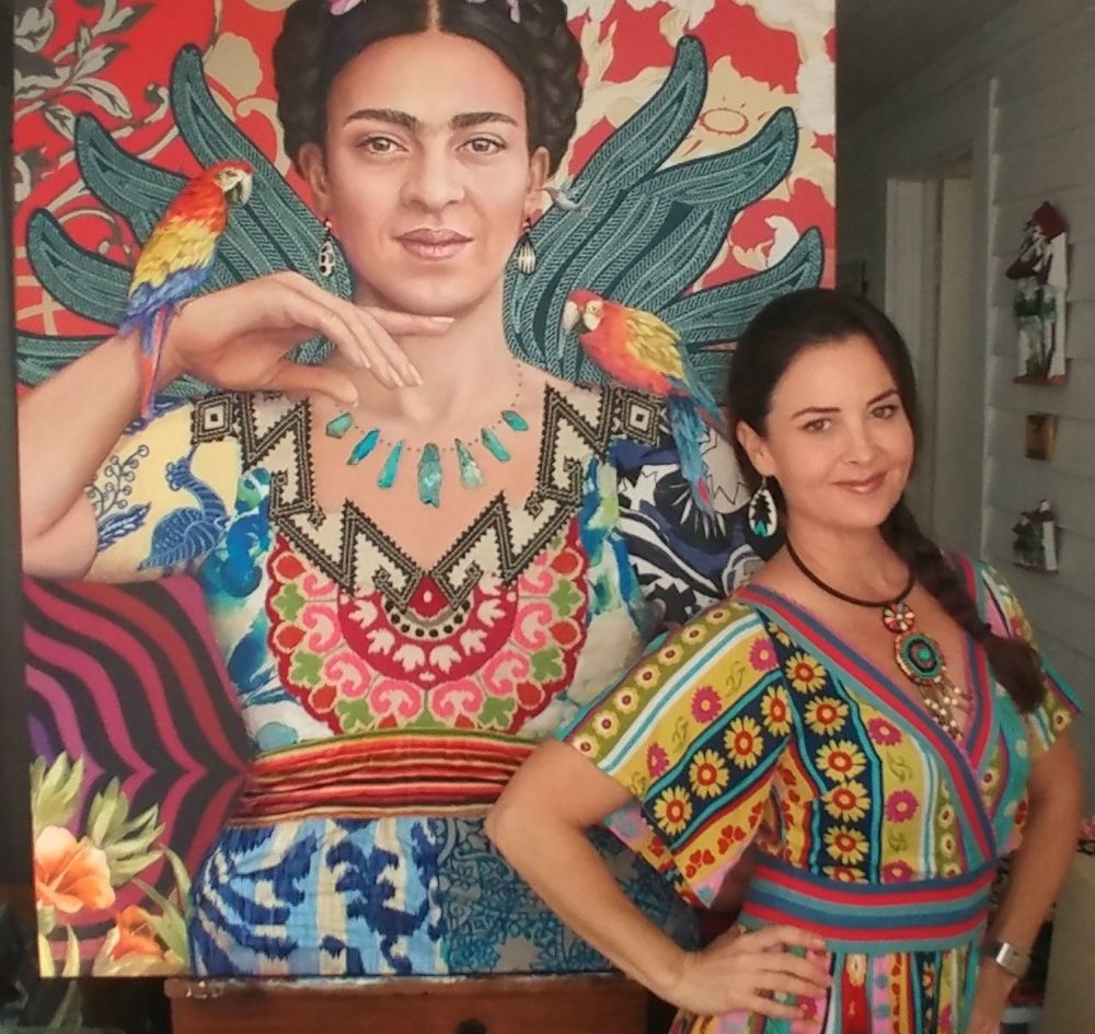 A woman in a colorful dress poses, smiling, next to a vibrant mural of Frida Kahlo with parrots on her shoulders in Fort Lauderdale. Both wear bold patterns and jewelry, celebrating the artistry and spirit of Hispanic Heritage Month. The background features bright, intricate designs that pay homage to history and cultural richness. Lifestyle