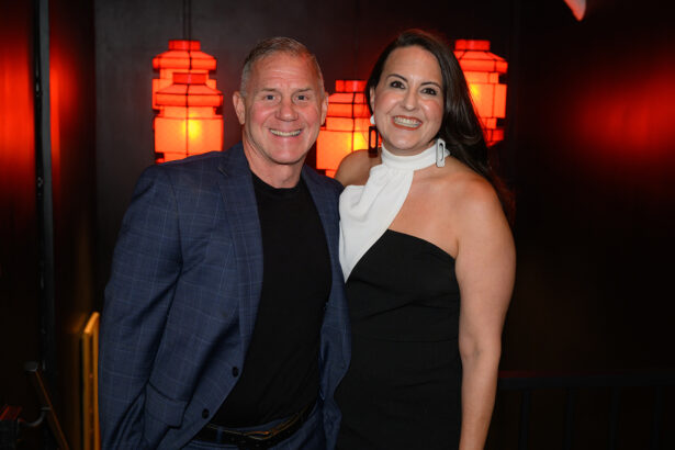 A man in a blue blazer and a woman in a black and white dress smile together in front of red lantern-shaped lights on a dark wall. Lifestyle