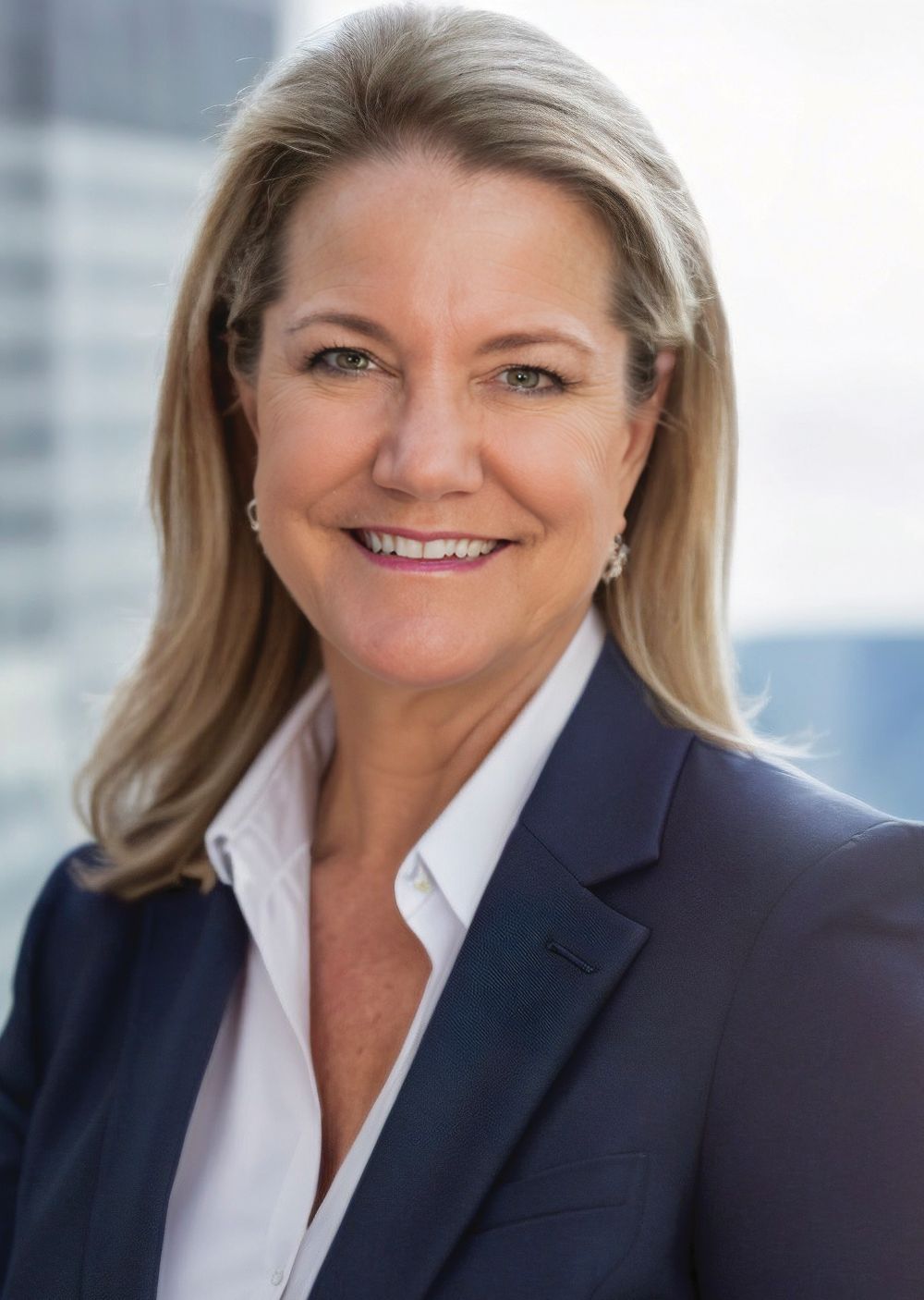 A woman with long blonde hair wearing a navy blazer and white shirt smiles at the camera, exuding a confident business demeanor. The background shows an out-of-focus modern building. Lifestyle