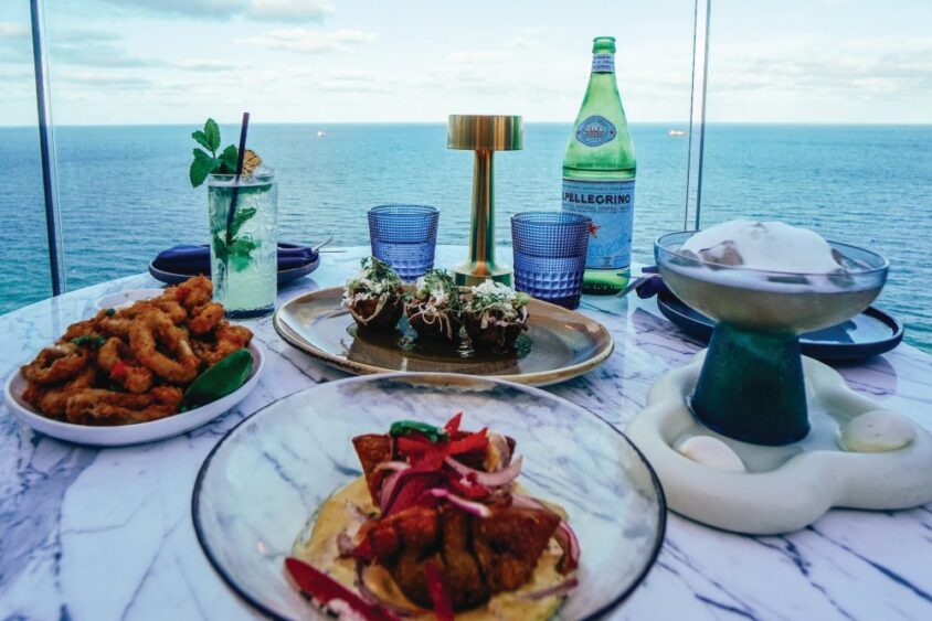 Appetizers, cocktails, and a bottle of San Pellegrino on a table overlooking the ocean at a boat show restaurant. Lifestyle