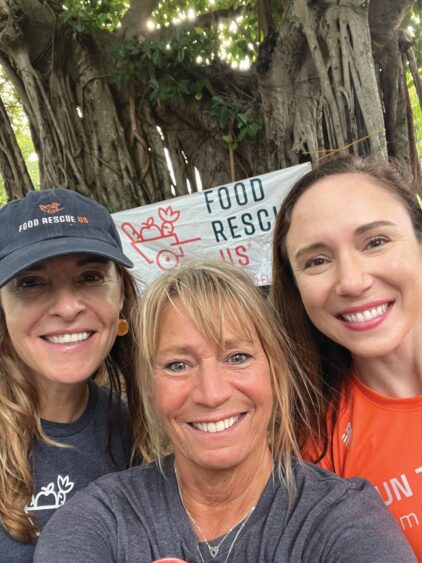 Three women smiling in a selfie in front of a Food Rescue US banner while volunteering for food rescue. Lifestyle